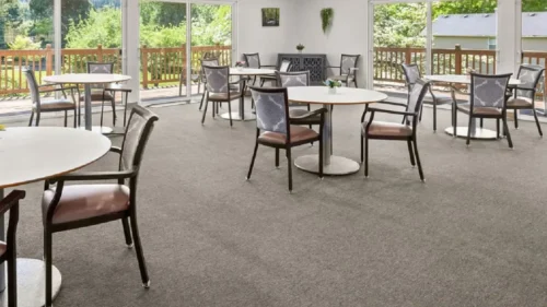 A cropped view of a dining room with multiple round tables, chairs with patterned backs, and a large sliding glass door opening to a deck