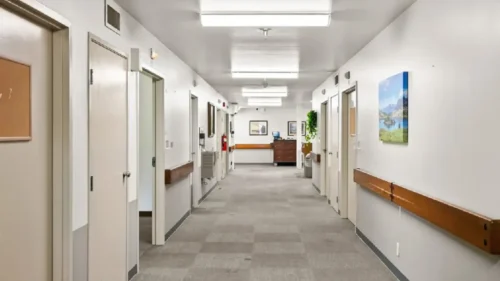 A long hallway with a checkered gray carpet, white walls, handrails, and closed doors on both sides